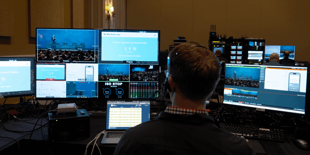 Recording at the Ligonier National Conference A man sits facing away from the camera, with 5 computer screens in front of him. He sits in a dimly lit room with other production personnel.