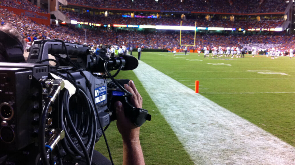 Professional cameraman filming a football game from the sidelines in a stadium