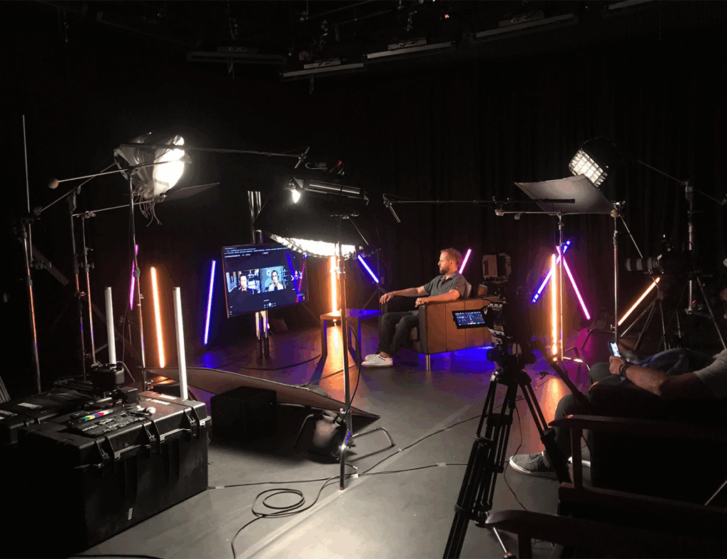 Image showing: A man siting in an arm chair, surrounded by professional video equipment, waiting to be interviewed.